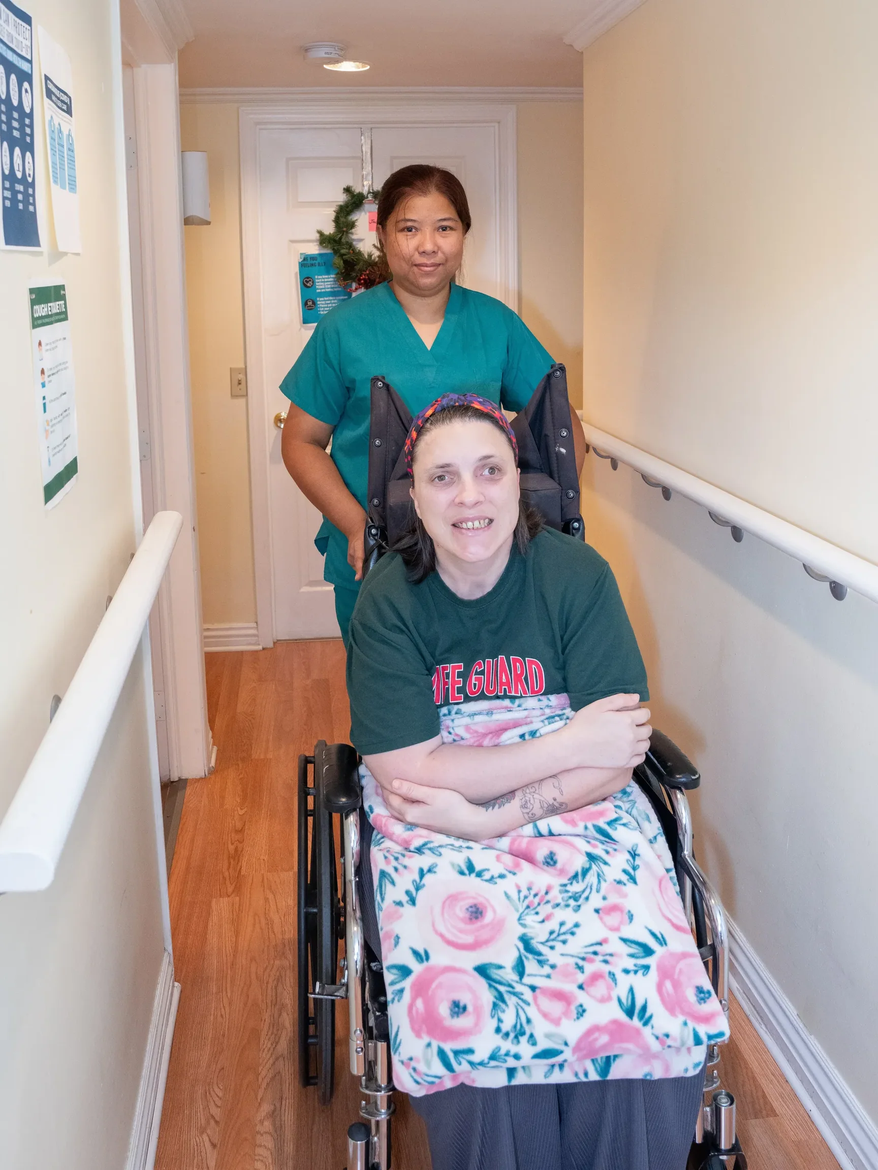 Caregiver assisting resident in wheelchair through accessible hallway with safety handrails