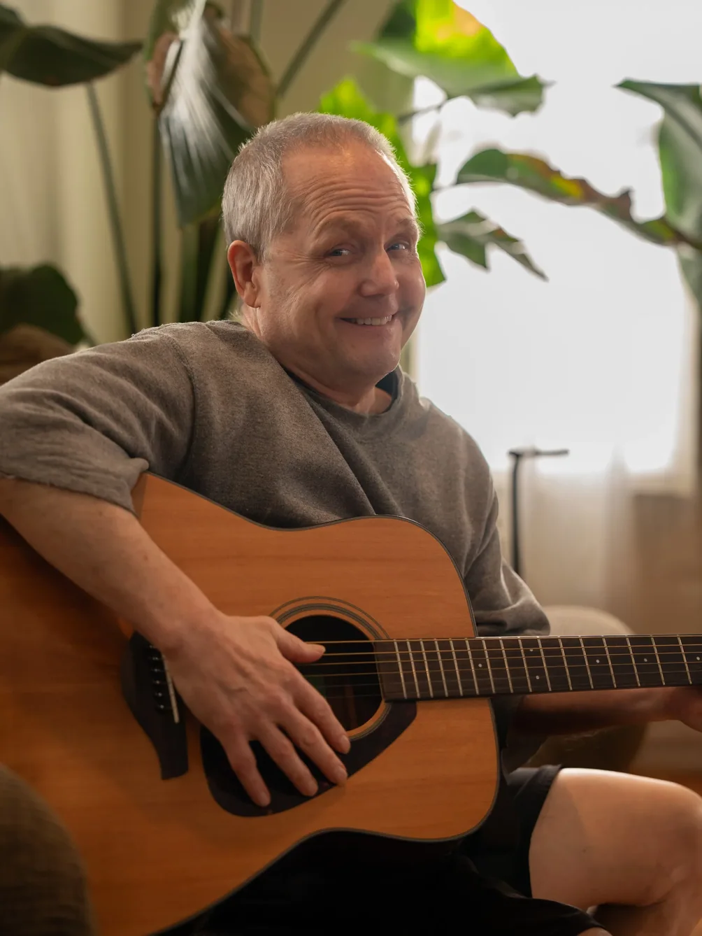 Resident enjoying music therapy while playing acoustic guitar in comfortable home setting